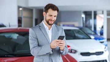 Business man in an automotive dealership using his cell phone.