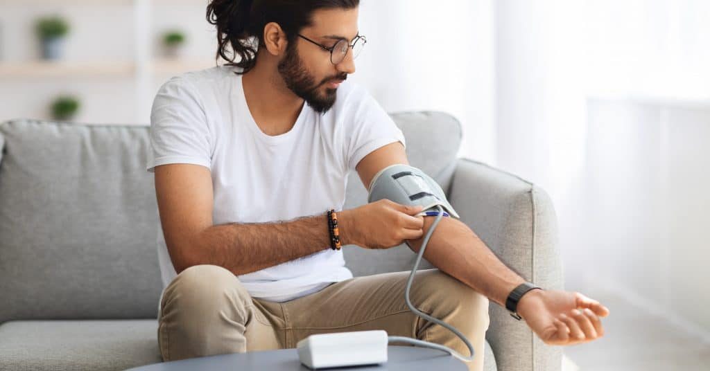 image of man on couch checking his blood pressure with medical device