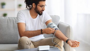 image of man on couch checking his blood pressure with medical device