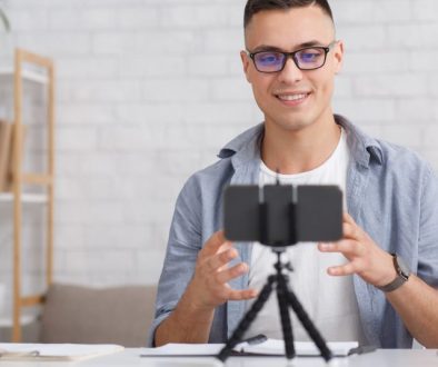 a man sits at a desk smiling into a smartphone on a tripod
