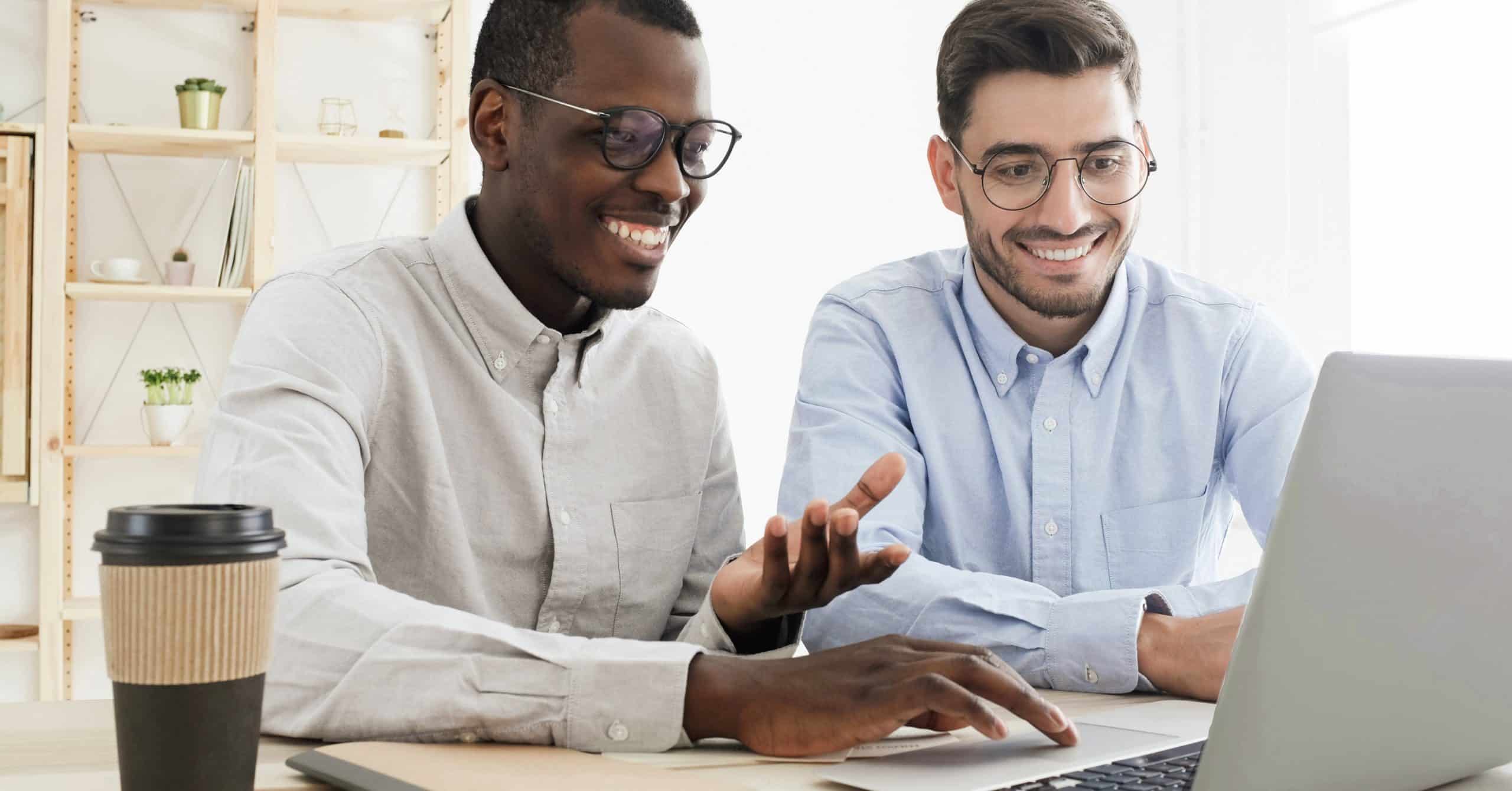 Two men dressed professionally and smiling gesture into a computer screen